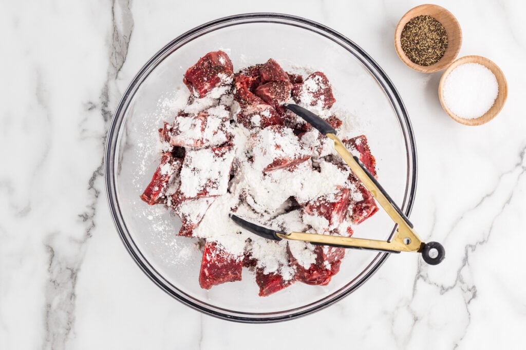 Chunks of raw beef coated with seasoning and cornstarch in a glass mixing bowl.