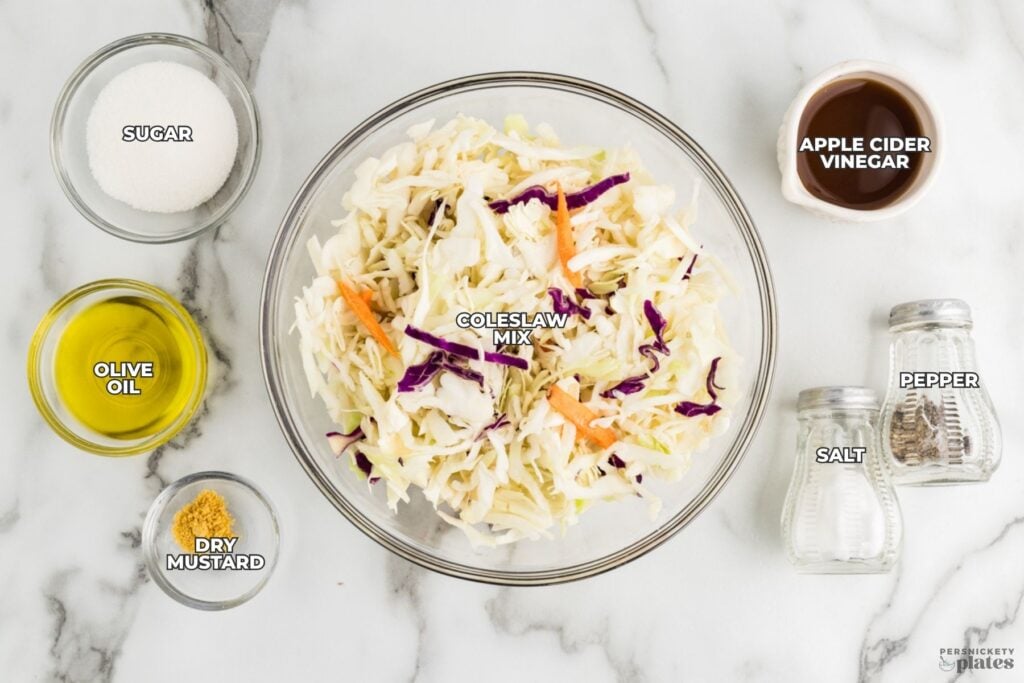 Ingredients for vinegar coleslaw arranged on a countertop around a bowl of coleslaw mix.
