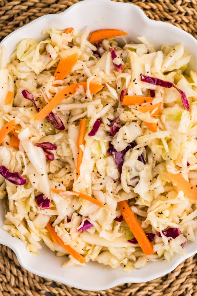 The coleslaw contains shredded green cabbage, purple cabbage, and carrot strips tossed in a light dressing and sprinkled with black pepper.