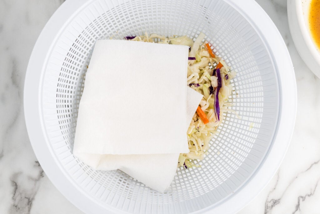 Overhead view of shredded cabbage, purple cabbage, and carrot strips inside a white salad spinner.