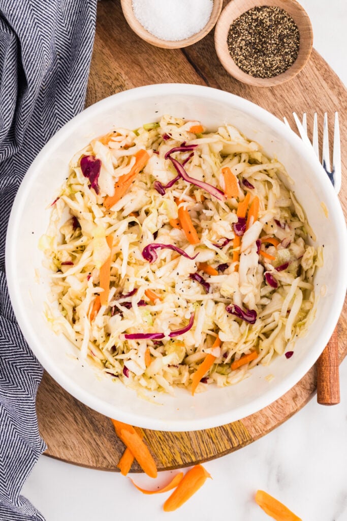 Vinegar coleslaw in a white bowl with salt, pepper, and a serving fork nearby.