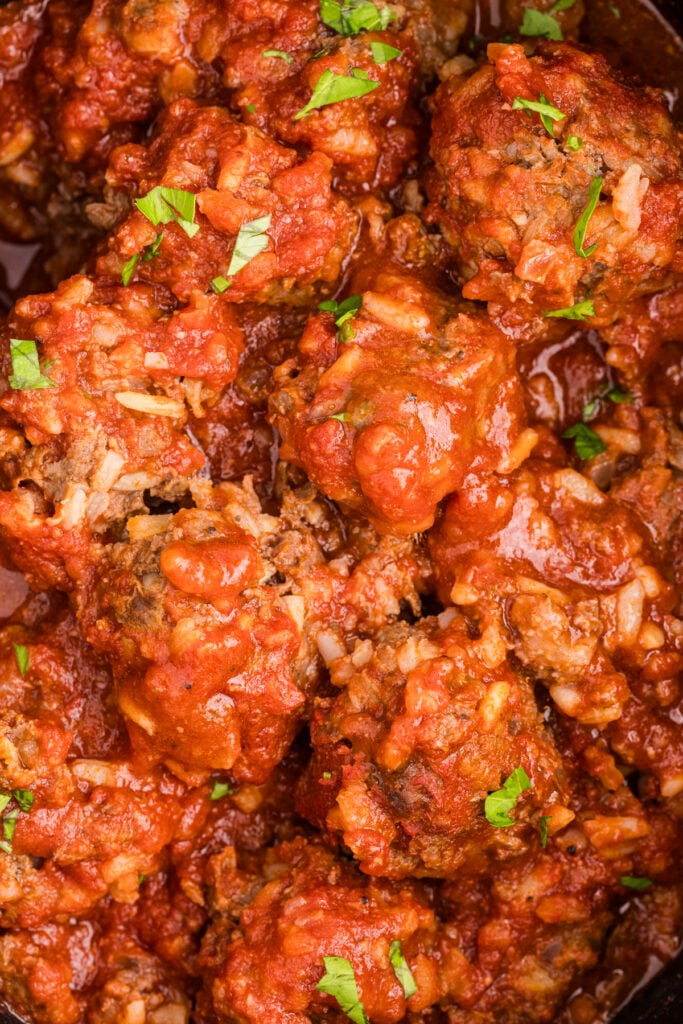 Close-up of slow cooker porcupine meatballs coated in tomato sauce and sprinkled with chopped parsley.