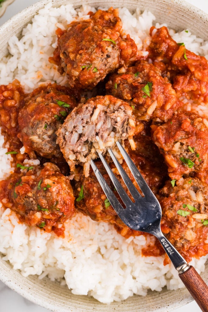 Porcupine meatballs served over white rice with a fork holding a cut-open meatball.