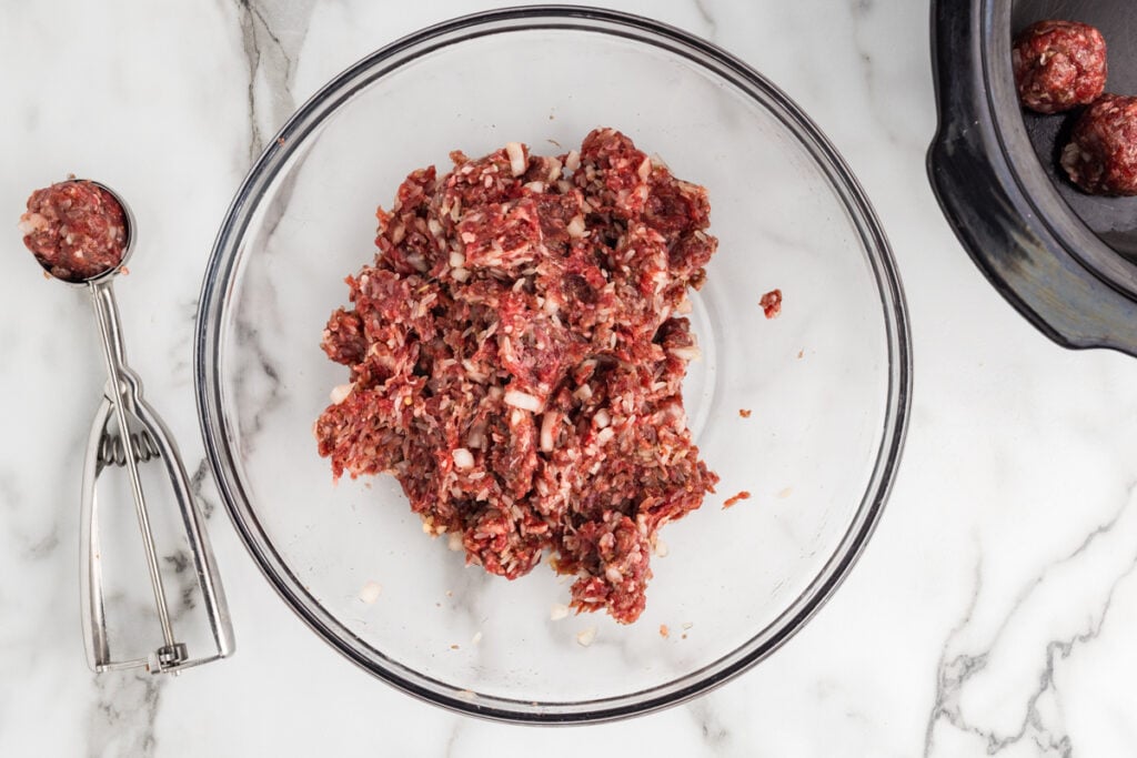 Glass bowl of mixed porcupine meatball mixture with a cookie scoop beside it.